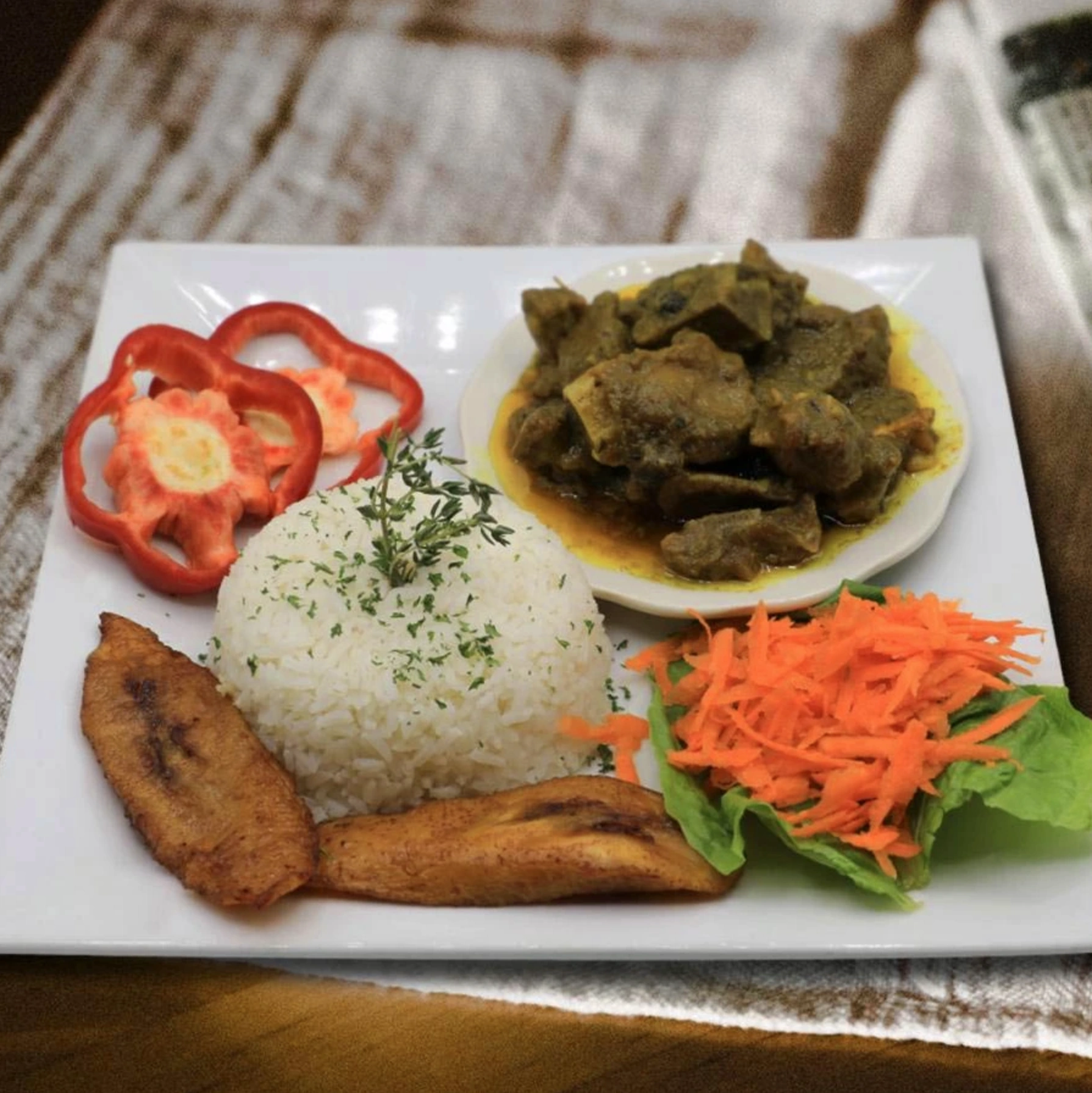Rice dish with plantain slices, salad, slices of red pepper and a small plate of meat in sauce